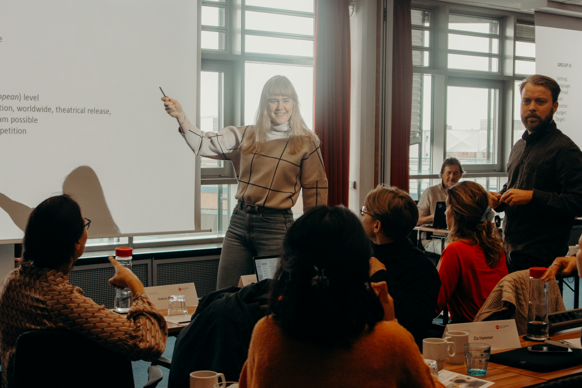 Teilnehmende beim Workshop, Frau zeigt auf einer Leinwand etwas den anderen, fröhliche Stimmung