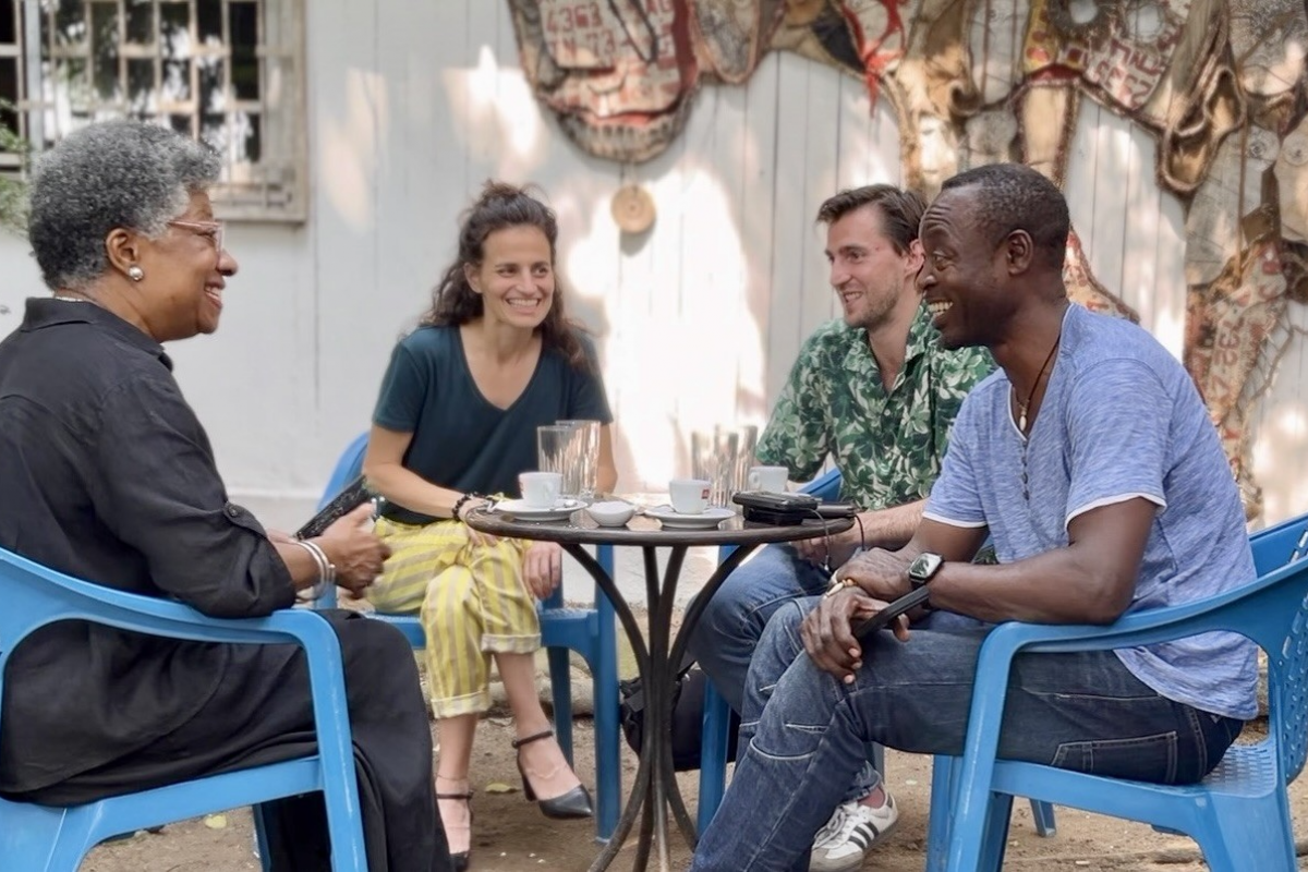 Vier MEnschen sitzen auf Plastikstühlen einander zugewandt und lachen, unterhalten sich.